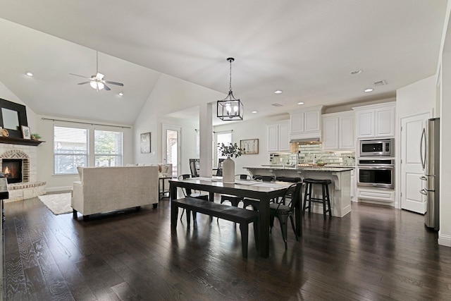 dining space with ceiling fan, lofted ceiling, dark wood-type flooring, and a fireplace