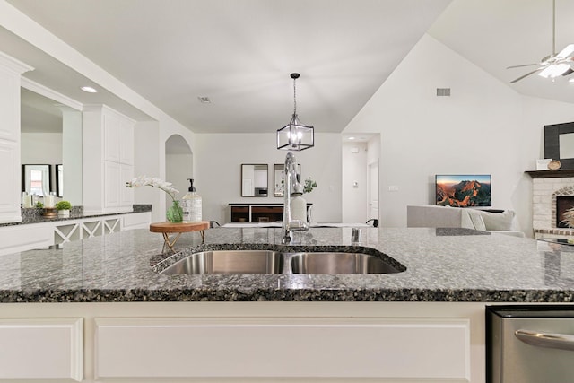 kitchen featuring pendant lighting, a fireplace, sink, dark stone countertops, and a center island with sink