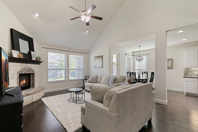 living room with high vaulted ceiling, a stone fireplace, ceiling fan with notable chandelier, and dark hardwood / wood-style flooring