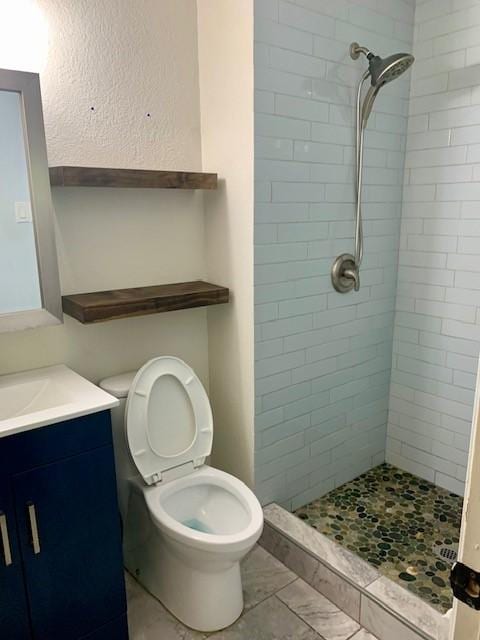 bathroom with vanity, toilet, and a tile shower