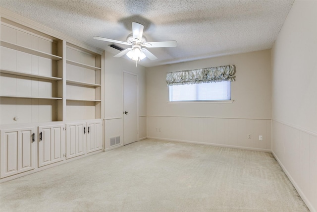 spare room featuring light colored carpet, ceiling fan, built in shelves, and a textured ceiling