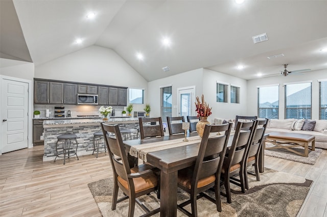 dining area with high vaulted ceiling, ceiling fan, and light wood-type flooring