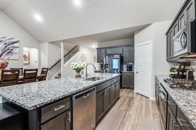 kitchen featuring sink, vaulted ceiling, light wood-type flooring, stainless steel appliances, and a kitchen island with sink