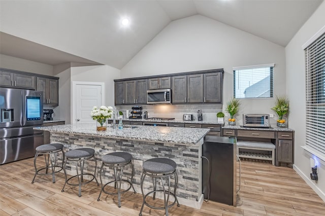 kitchen with a breakfast bar, a kitchen island with sink, light stone counters, stainless steel appliances, and dark brown cabinets