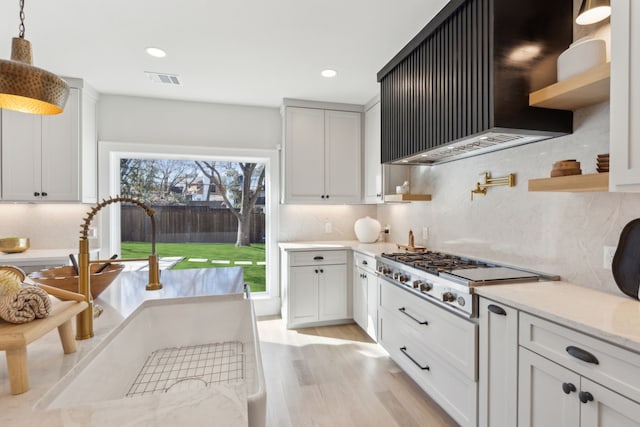 kitchen featuring pendant lighting, white cabinets, stainless steel gas stovetop, and wall chimney exhaust hood