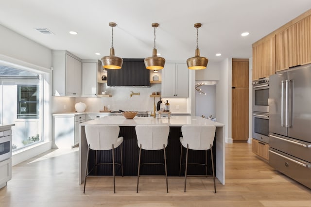 kitchen featuring white cabinetry, hanging light fixtures, stainless steel appliances, and a center island with sink