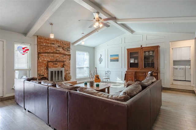 living room featuring independent washer and dryer, vaulted ceiling with beams, light hardwood / wood-style flooring, ceiling fan, and a fireplace