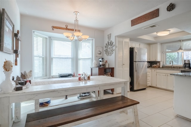 kitchen with pendant lighting, sink, light tile patterned floors, stainless steel refrigerator, and white cabinetry