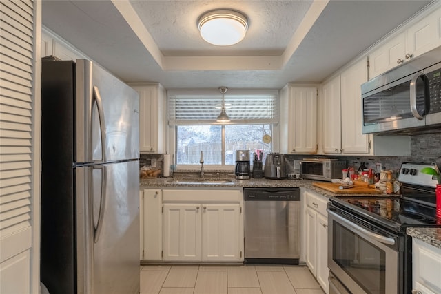 kitchen with appliances with stainless steel finishes, sink, dark stone counters, and white cabinets