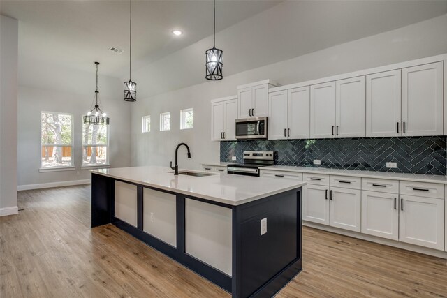 kitchen with appliances with stainless steel finishes, sink, a center island with sink, and decorative light fixtures