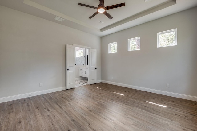 unfurnished bedroom featuring a tray ceiling, ensuite bathroom, and light wood-type flooring