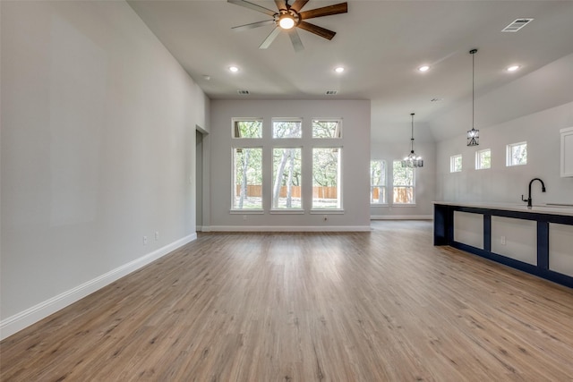 unfurnished living room with sink, ceiling fan with notable chandelier, high vaulted ceiling, and light hardwood / wood-style flooring