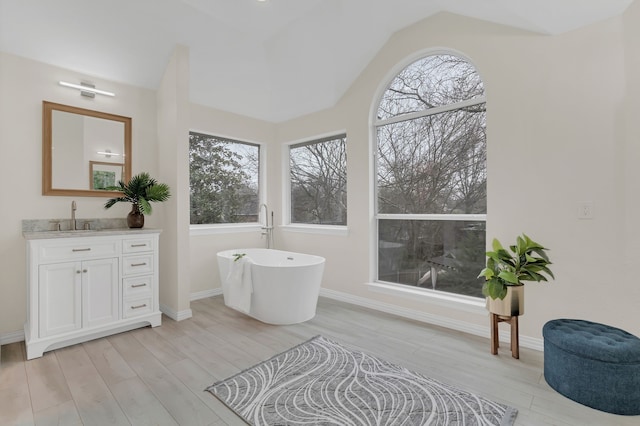 bathroom with lofted ceiling, a tub to relax in, hardwood / wood-style floors, and vanity