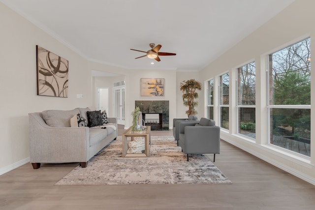 living room with ceiling fan, ornamental molding, a fireplace, and light hardwood / wood-style flooring