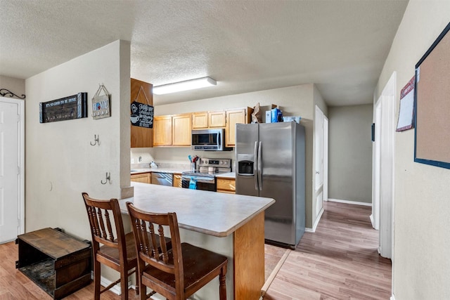 kitchen with kitchen peninsula, stainless steel appliances, light hardwood / wood-style floors, and a textured ceiling