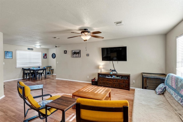 living room with ceiling fan, a textured ceiling, and light wood-type flooring