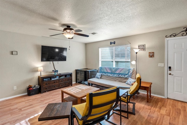 living room featuring ceiling fan, a textured ceiling, and light wood-type flooring