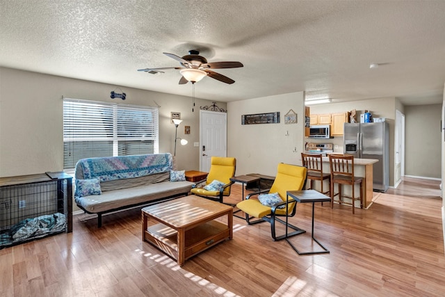 living room featuring ceiling fan, light hardwood / wood-style floors, and a textured ceiling