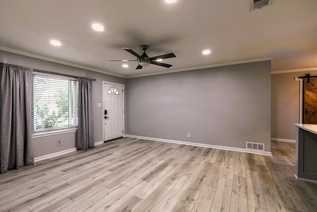 interior space featuring crown molding, a barn door, ceiling fan, and light hardwood / wood-style flooring