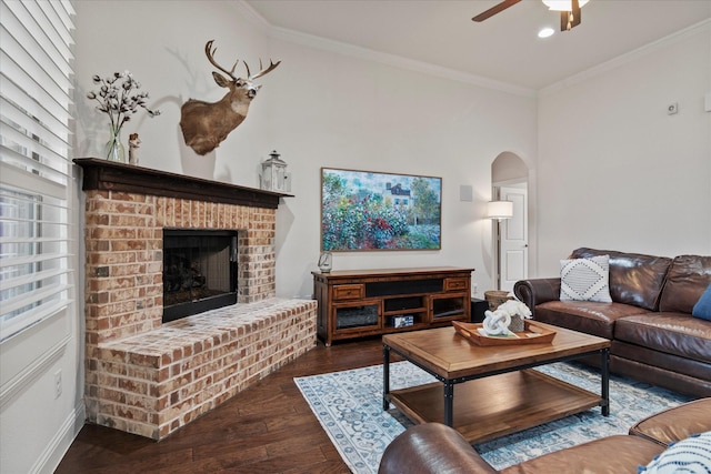 living room with dark wood-type flooring, ceiling fan, crown molding, and a brick fireplace