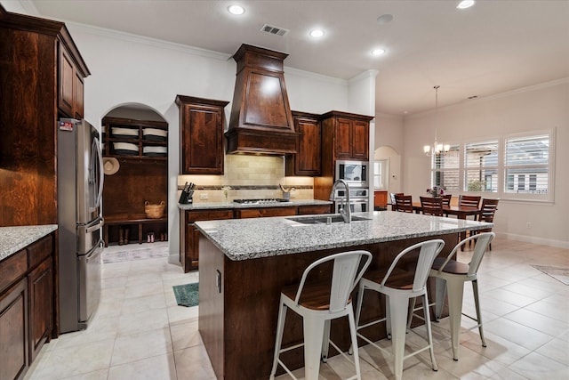 kitchen featuring premium range hood, stainless steel appliances, light stone countertops, and a center island with sink