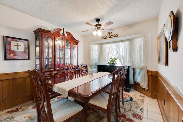 tiled dining space featuring ceiling fan, wooden walls, and a textured ceiling