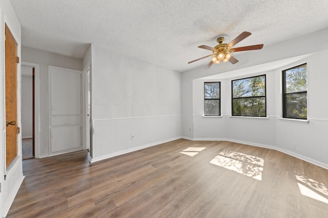 empty room featuring wood-type flooring, a healthy amount of sunlight, ceiling fan, and a textured ceiling