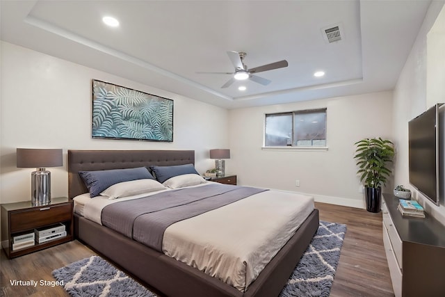 bedroom with baseboards, visible vents, dark wood-type flooring, a tray ceiling, and recessed lighting