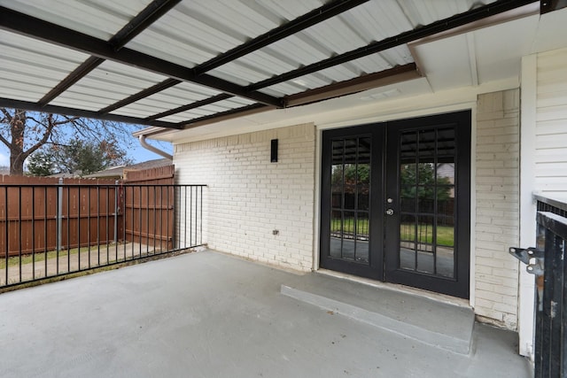 entrance to property featuring french doors, a patio area, fence, and brick siding