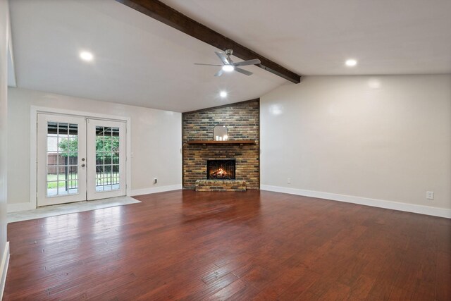 unfurnished living room with ceiling fan, vaulted ceiling with beams, a fireplace, dark hardwood / wood-style flooring, and french doors