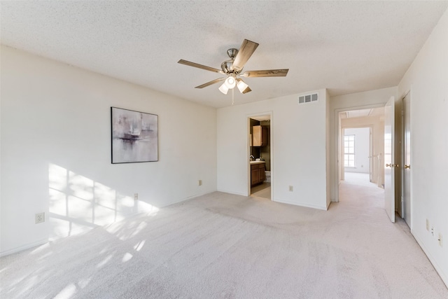 unfurnished bedroom featuring light carpet, ceiling fan, ensuite bath, and a textured ceiling