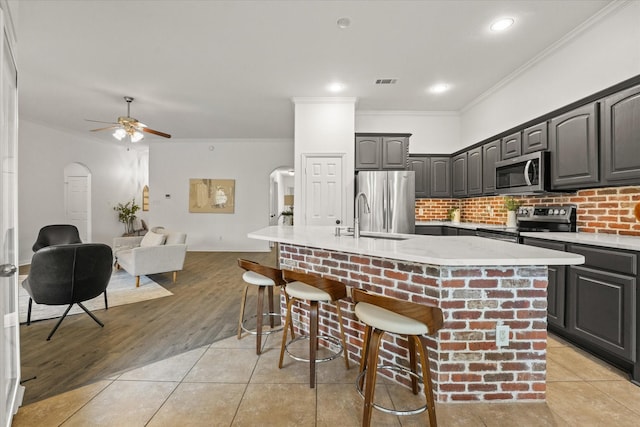 kitchen with sink, crown molding, a breakfast bar area, appliances with stainless steel finishes, and a kitchen island with sink