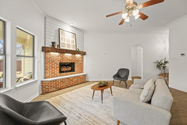 living room with ceiling fan, ornamental molding, wood-type flooring, and a fireplace