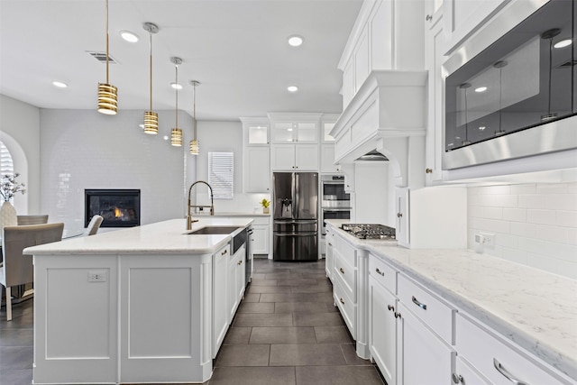 kitchen with an island with sink, white cabinetry, hanging light fixtures, light stone counters, and stainless steel appliances