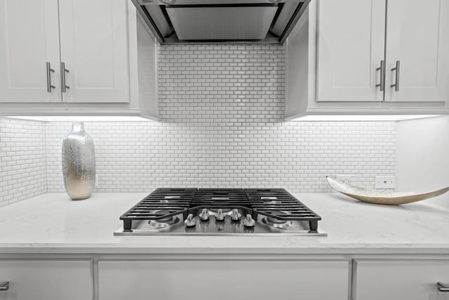 kitchen with ventilation hood, white cabinets, stainless steel gas stovetop, light stone countertops, and backsplash