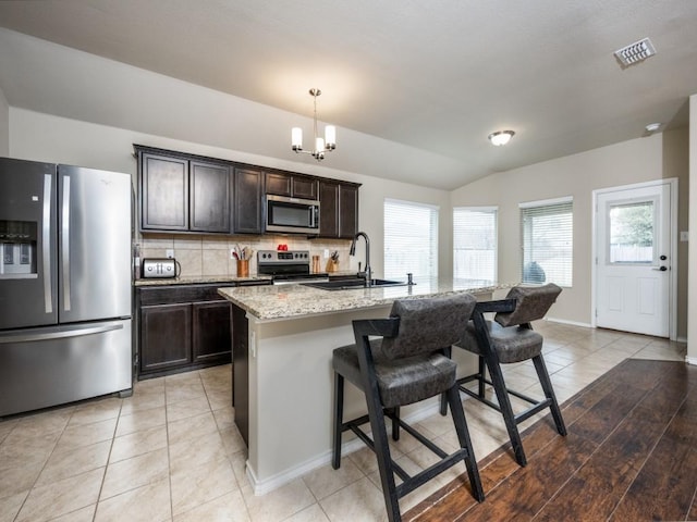 kitchen with sink, hanging light fixtures, an island with sink, stainless steel appliances, and light stone countertops