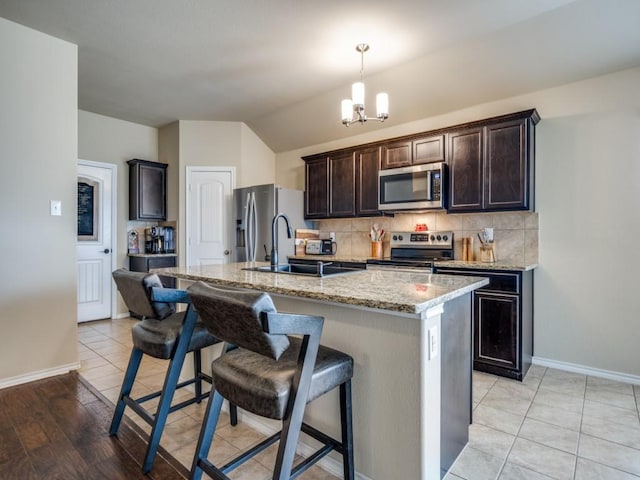 kitchen featuring light stone countertops, an island with sink, appliances with stainless steel finishes, and backsplash