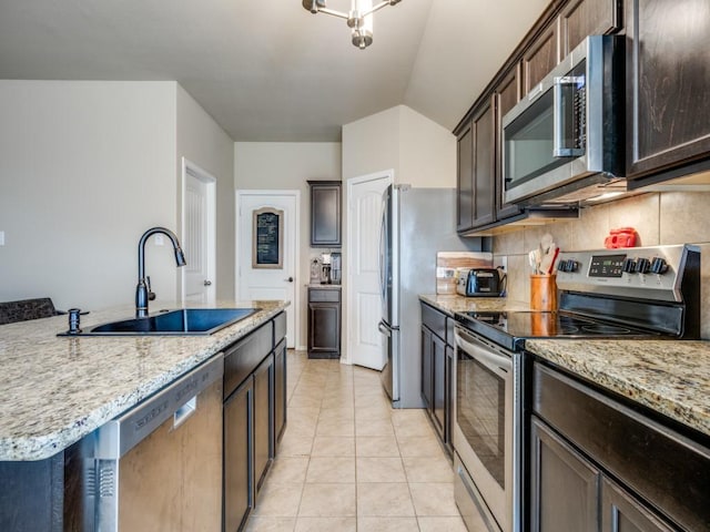 kitchen with sink, backsplash, stainless steel appliances, light stone countertops, and dark brown cabinets