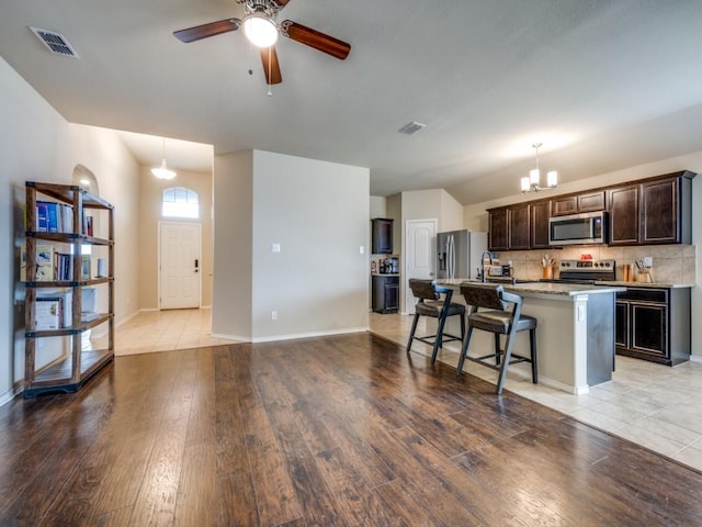 kitchen with a breakfast bar, appliances with stainless steel finishes, a kitchen island with sink, light hardwood / wood-style floors, and decorative backsplash