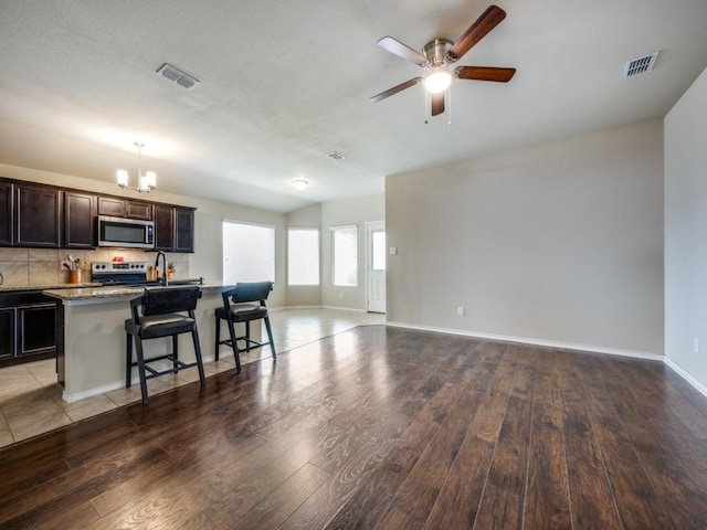 kitchen featuring stainless steel appliances, a kitchen island with sink, hardwood / wood-style floors, and a kitchen bar