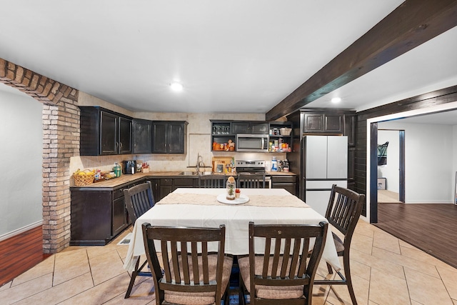 kitchen with light tile patterned floors, sink, appliances with stainless steel finishes, a kitchen island, and beamed ceiling