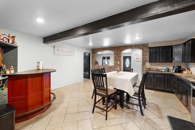 dining room with wet bar, light tile patterned flooring, beamed ceiling, and brick wall