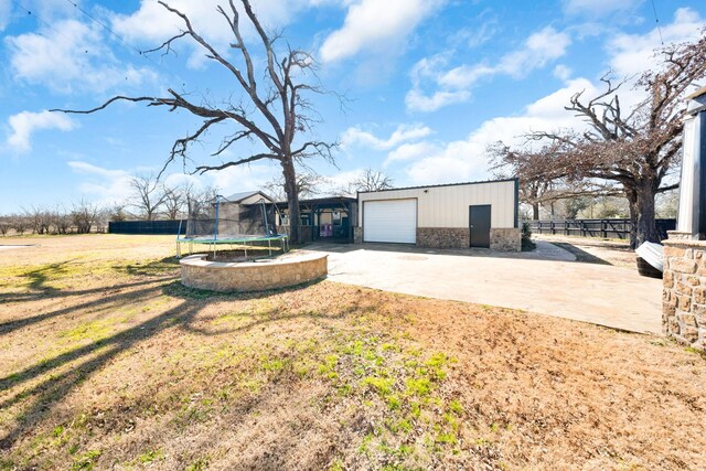 exterior space featuring a garage, an outbuilding, a trampoline, and a front lawn