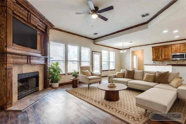 living room with crown molding, ceiling fan, a tile fireplace, and light wood-type flooring