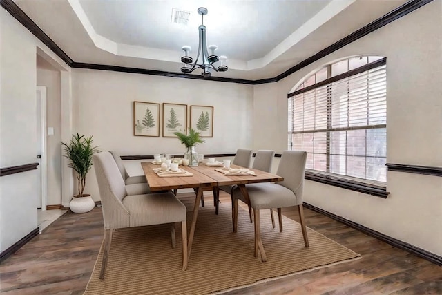 dining area featuring a raised ceiling, ornamental molding, dark wood-type flooring, and an inviting chandelier