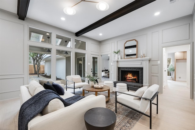 living room with beamed ceiling, light hardwood / wood-style floors, and a brick fireplace