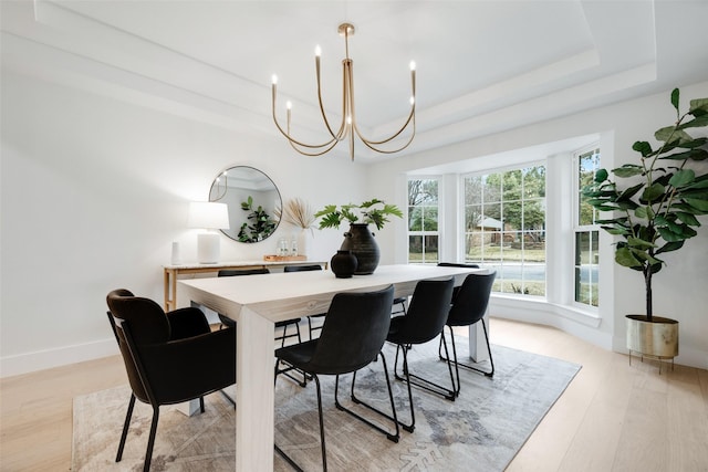 dining room with light hardwood / wood-style floors, a raised ceiling, and a chandelier