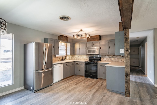 kitchen featuring gray cabinetry, decorative backsplash, hanging light fixtures, stainless steel appliances, and light wood-type flooring