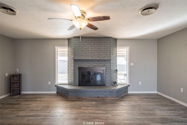 unfurnished living room featuring a brick fireplace, a healthy amount of sunlight, dark wood-type flooring, and a textured ceiling