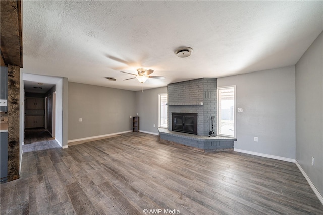 unfurnished living room with dark hardwood / wood-style floors, ceiling fan, a fireplace, and a textured ceiling